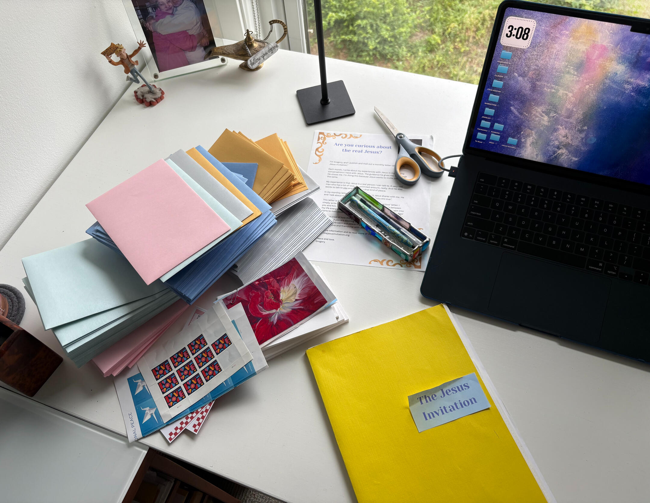 Stacks of colored envelopes, Love and Peace postage stamps, and a folder labeled The Jesus Invitation, ready for mailing